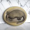 Oval-shaped Western belt buckle with a 3D armadillo design, featuring an antique brass finish and rustic detailing.