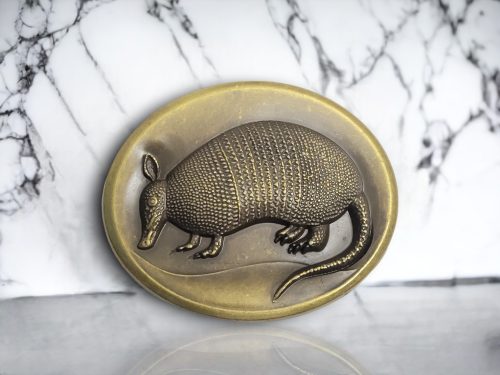 Oval-shaped Western belt buckle with a 3D armadillo design, featuring an antique brass finish and rustic detailing.