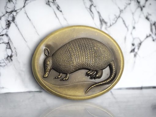 Oval-shaped Western belt buckle with a 3D armadillo design, featuring an antique brass finish and rustic detailing.