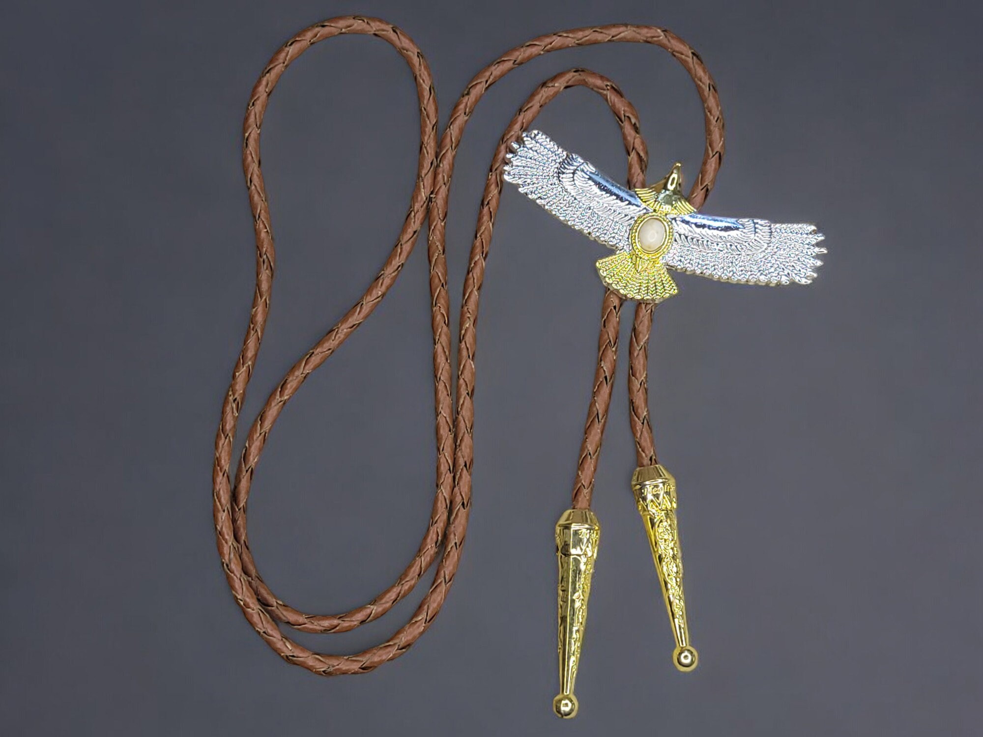 2 Tone Metal Soaring Eagle with Braied Cowhide Leather Bolo Tie (9) Two-tone gold and silver American eagle bolo tie with braided leather cord, metal tips, and an adjustable slider clasp.