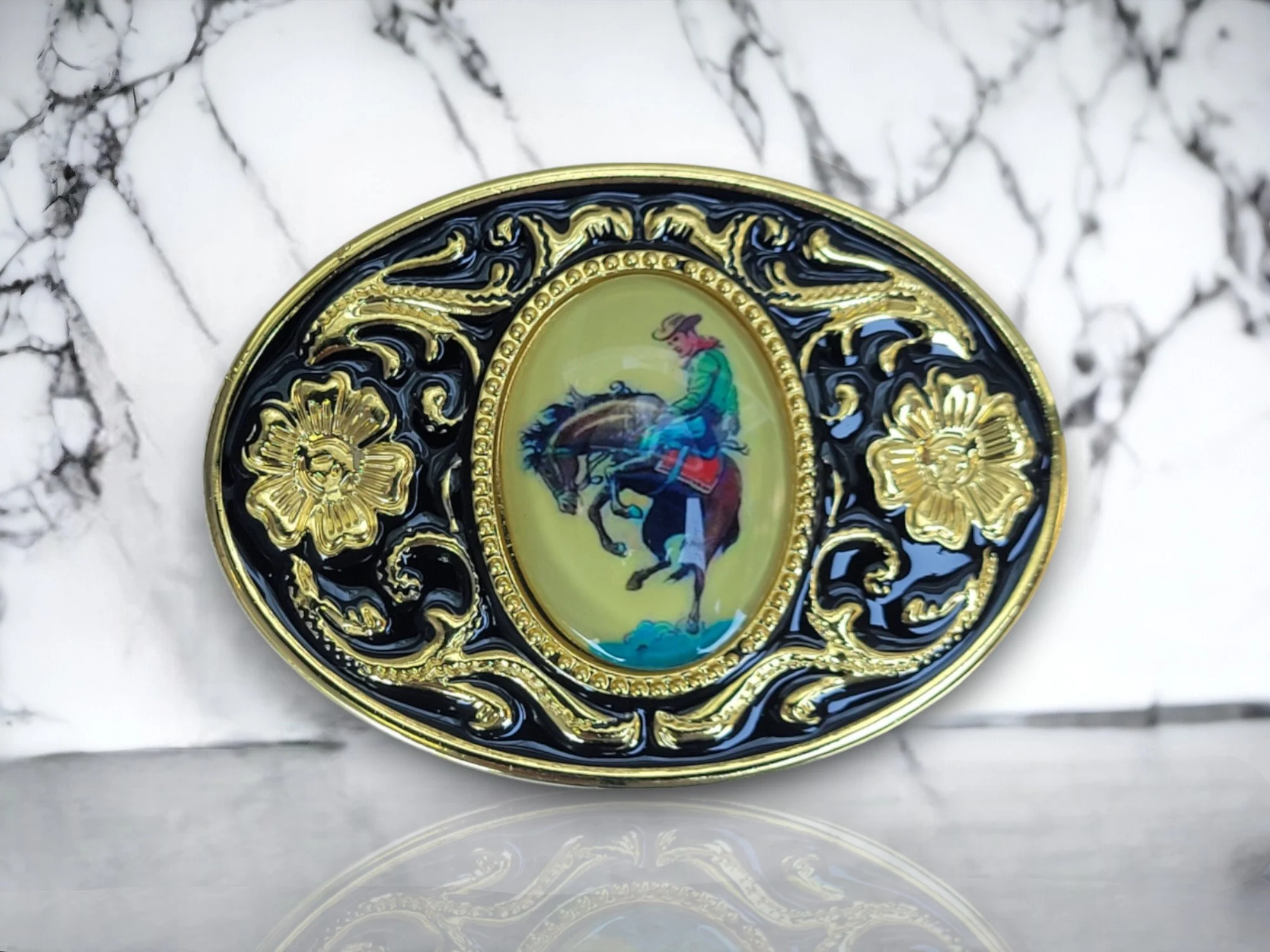 Western belt buckle featuring a cowboy riding a bronco, surrounded by a gold and black
