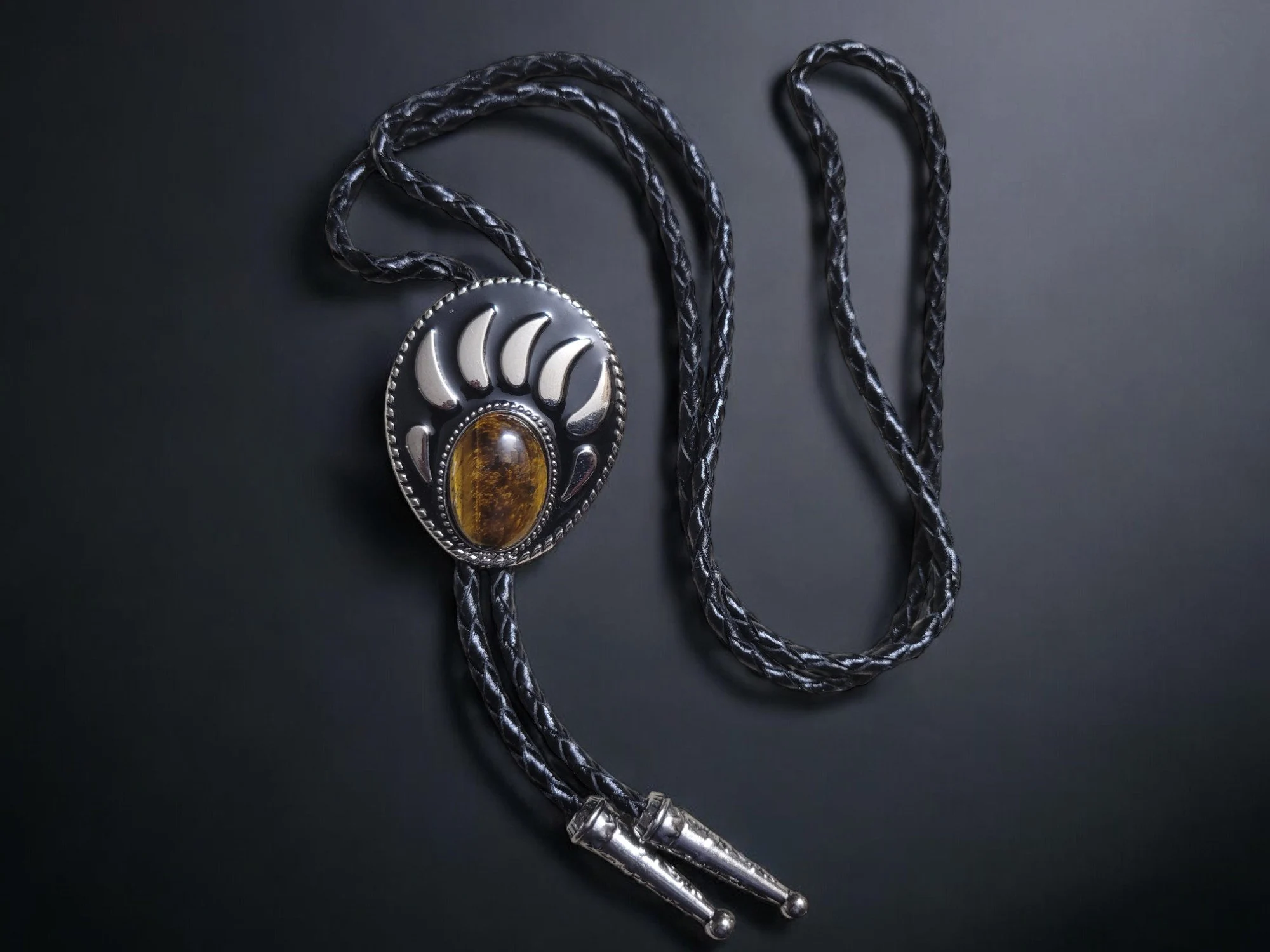 Western-style bear claw bolo tie with a tiger eye gemstone, braided leather cord, and metal tips.