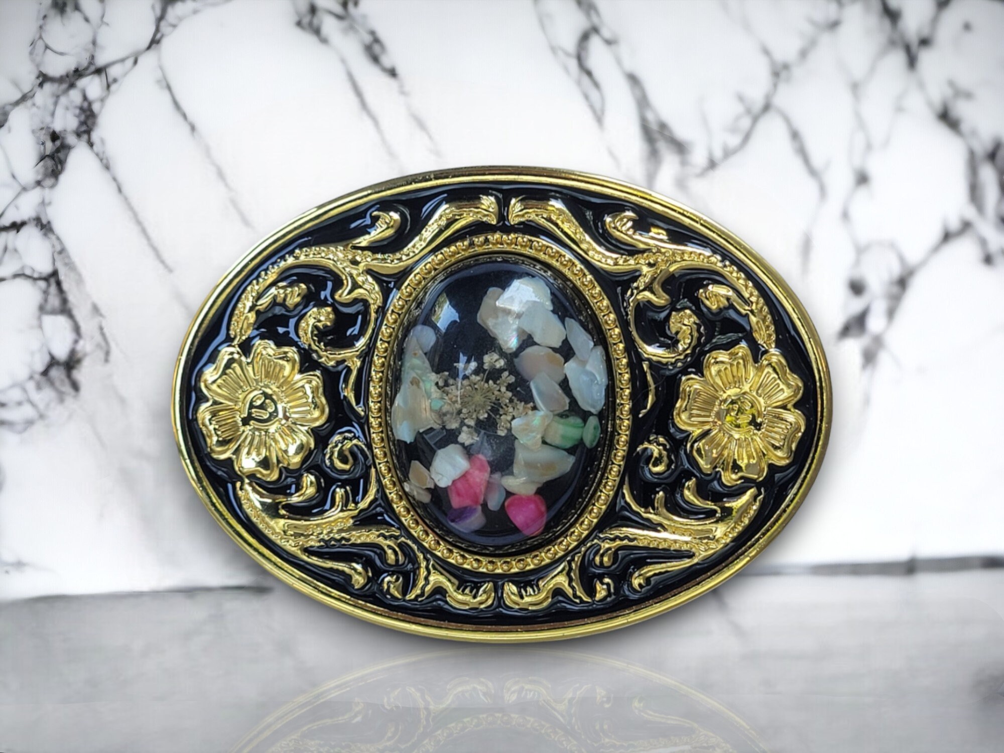 Western belt buckle with resin-protected raw gemstone featuring a gold and black enamel floral design, crafted from durable metal alloy for a stylish look.
