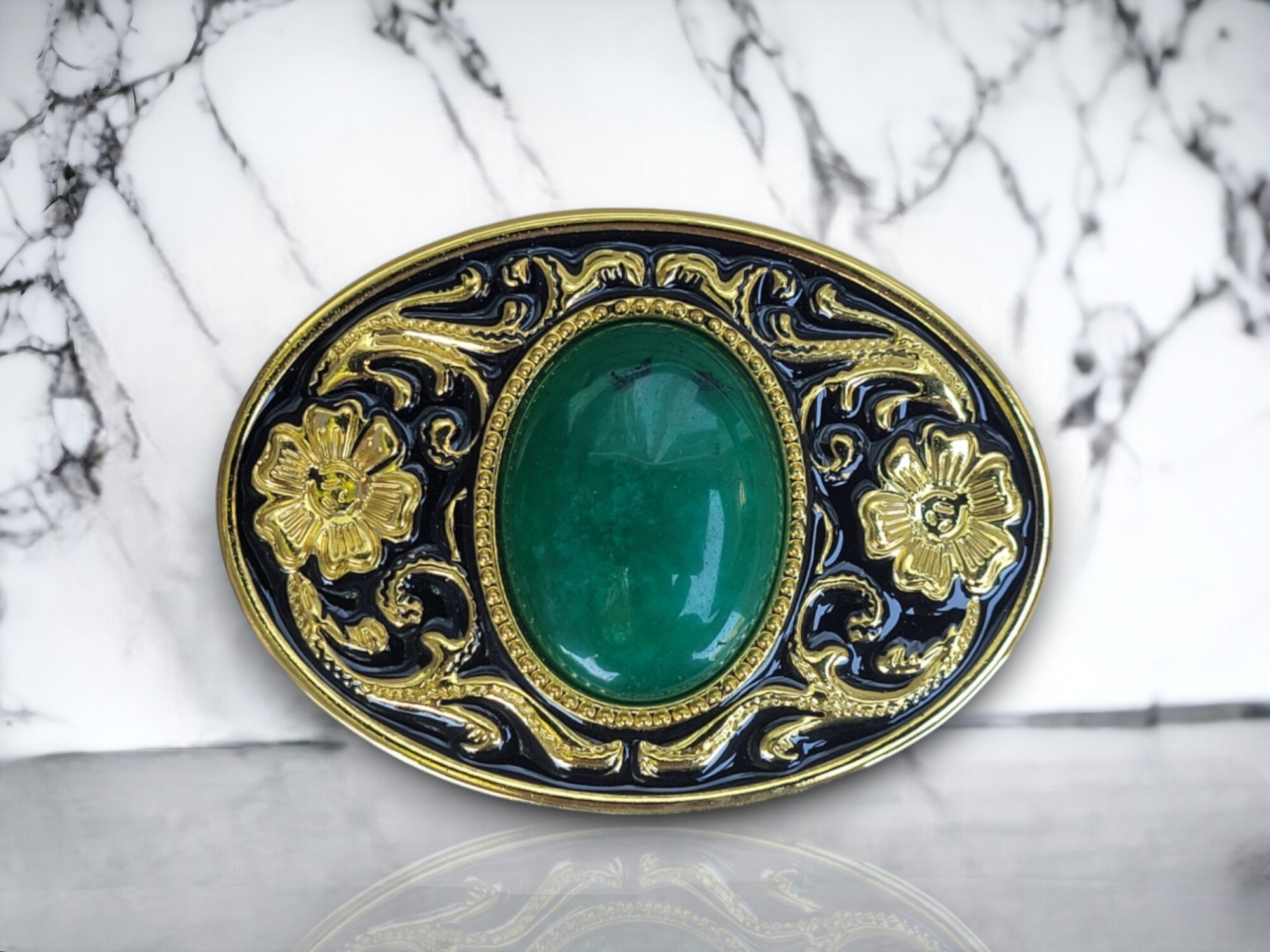 Western-style belt buckle with a large oval jade centerpiece, gold and black enamel floral design, and a polished metal alloy finish.